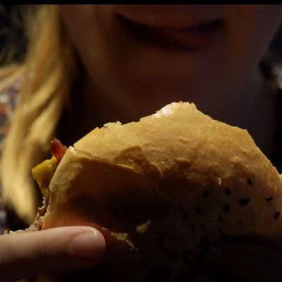 close up of a woman's face. She's holding a hamburger and licking her lips 